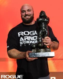 Strongman holding an Arnold Strongman Classic trophy.