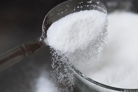 Sugar pouring from a spoon into a bowl.
