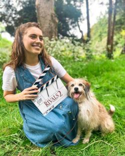 Woman holding a clapperboard for Rivals 2 with a dog.