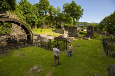 Two people talking near historic ruins and a water wheel.