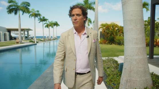 Stephen Mangan walking by a resort pool.