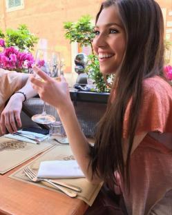 Woman sitting at an outdoor cafe table, holding a glass of wine.