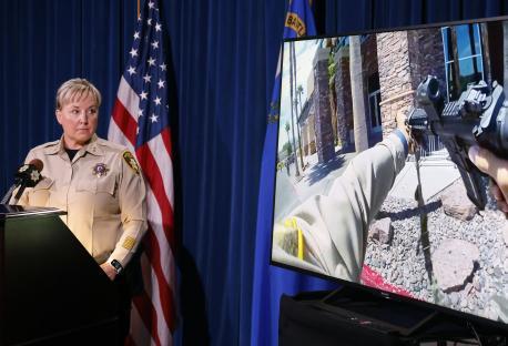 Bodycam footage of a police officer aiming a weapon is shown on a screen as a police official speaks at a press conference.