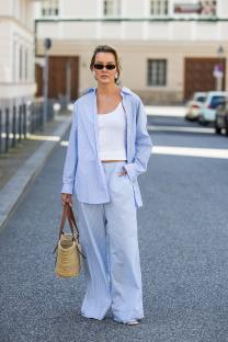 Woman in blue striped pants and shirt, sunglasses, and a straw bag.