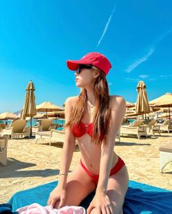 Woman in red bikini and sunglasses sitting on a beach towel.