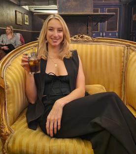 Woman sitting in an ornate chair, holding a drink.