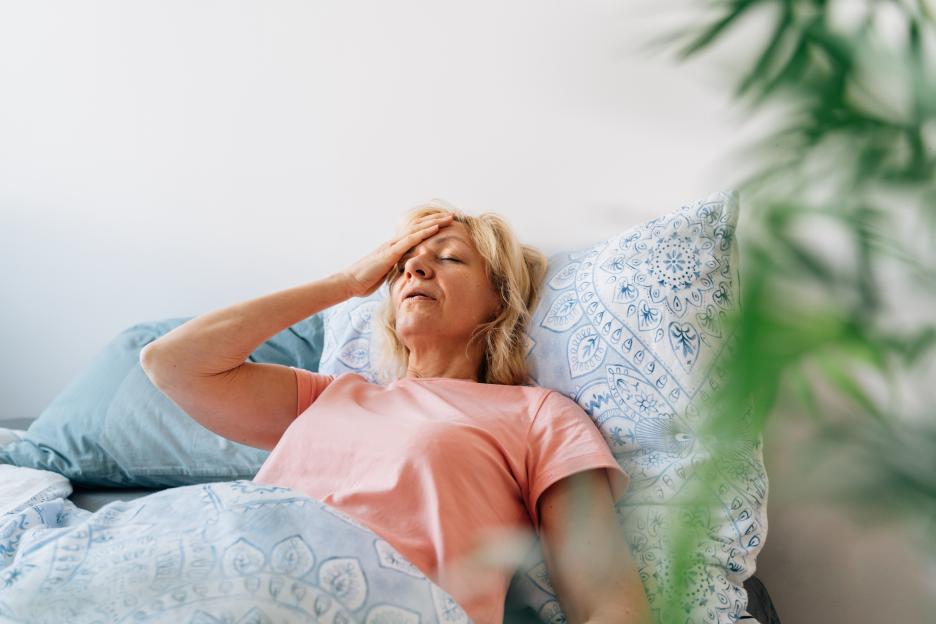 A middle-aged woman lying in bed, experiencing hot flashes.