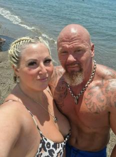 Couple on a beach; the man has tattoos and is shirtless.