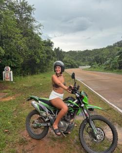 Young woman sitting on a green motorcycle on a road.