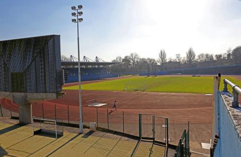Disrepair of Crystal Palace National Sports Centre, showing track, stands, and a runner.