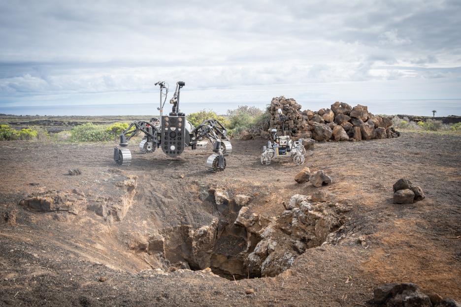 Two robots near a lava tube on Lanzarote, testing equipment for exploring caves on the Moon and Mars.