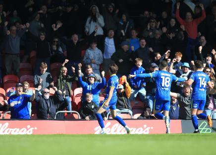 AFC Wimbledon players celebrating a goal in front of cheering fans.