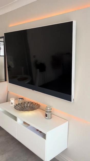 Large TV mounted on wall above white media console with decorative items.