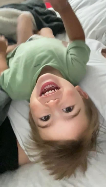 A child lying upside down, laughing into the camera.