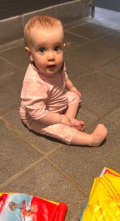 Baby girl sitting on the floor wearing a pink polka dot swimsuit.
