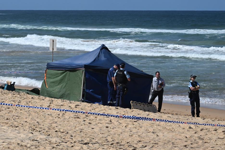 Police officers at a beach investigating a fatal shark attack.
