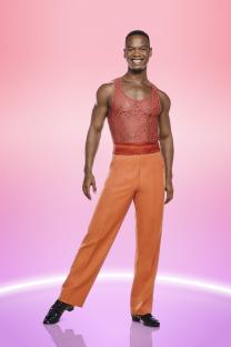 Johannes Radebe in orange dance attire for Strictly Come Dancing.