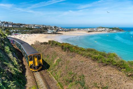 Train traveling along a coastal railway line overlooking a beach and town.