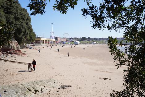 People enjoying a sunny day at a beach with amusement park rides in the background.