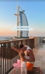 Man kneeling and kissing his daughter with Burj Al Arab in the background.