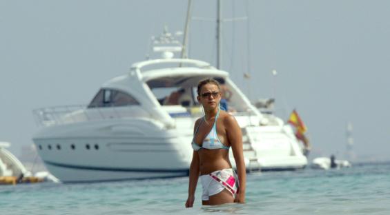 a woman in a bikini stands in the water with a boat in the background