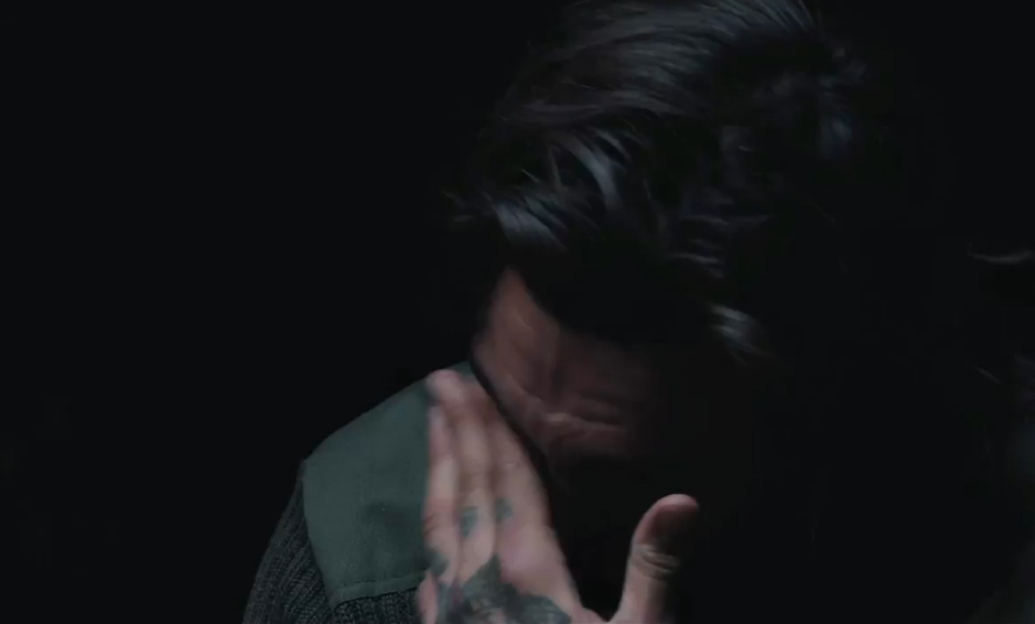 Close-up of a man with tattoos on his hand, touching his face.