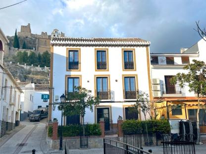 White building in a Spanish town with a castle in the background.