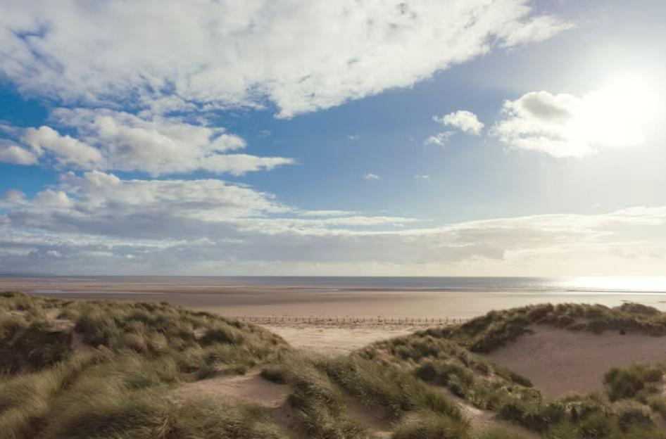 Sandy beach with dunes and a partly cloudy sky.