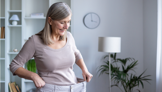 Woman holding up loose pants after weight loss.