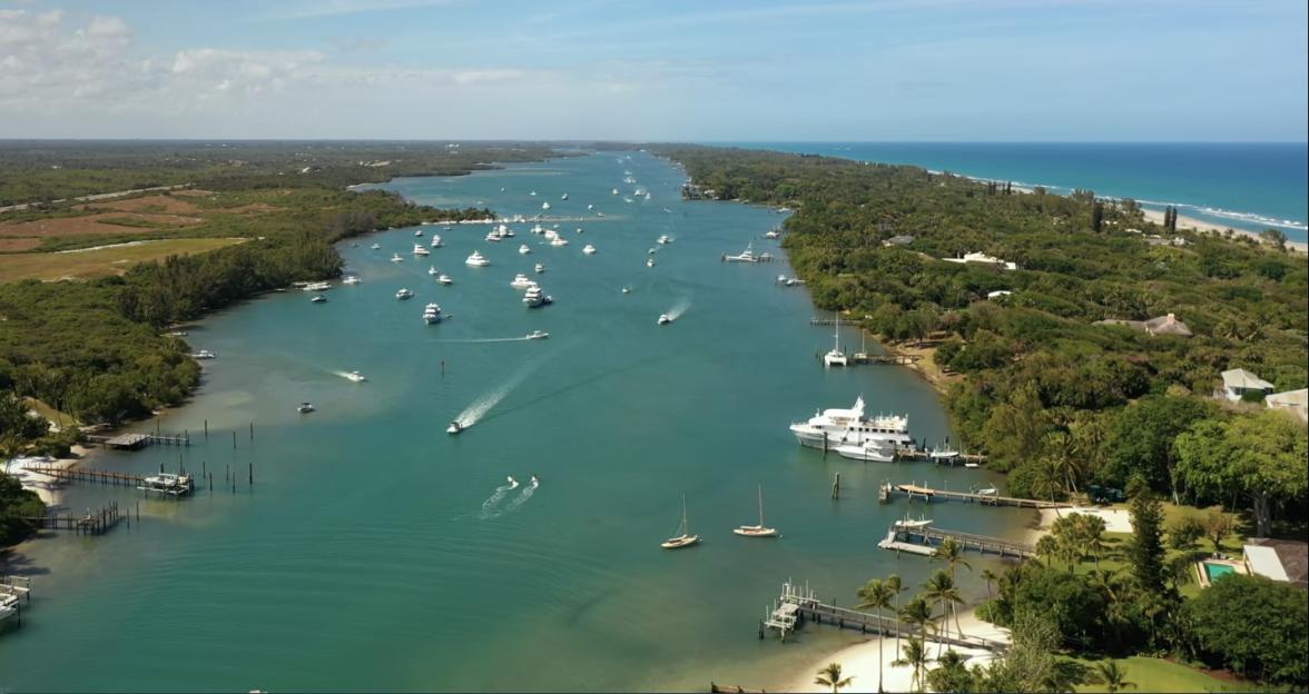 Aerial view of Jupiter, Florida, showing boats in a waterway surrounded by lush green land with the ocean visible in the background.