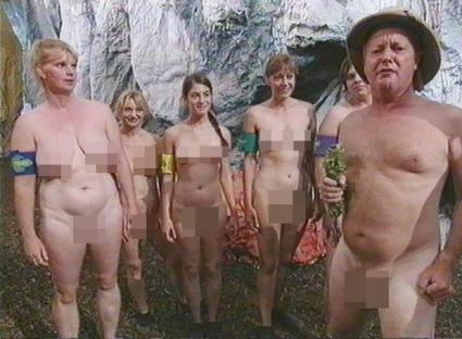 Group of nude adults standing in front of a rock wall.