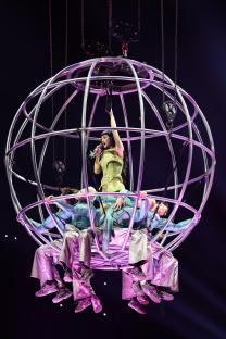 Katy Perry performing onstage in a large spherical cage with backup dancers.