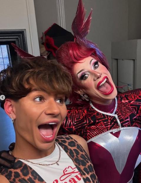 Sam Ashby and a drag queen in red wig and costume, both with mouths open in excitement.
