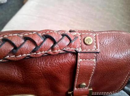 Close-up of a brown leather handbag with braided detail.