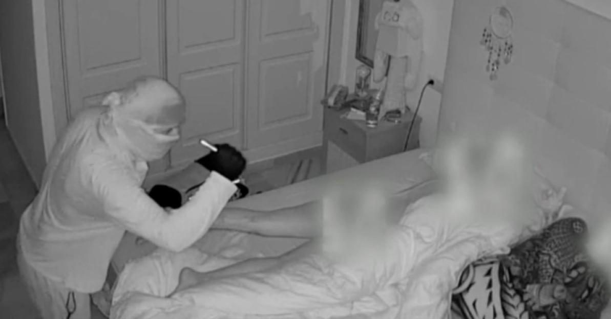 Security camera footage of a masked person stealing from a sleeping person.