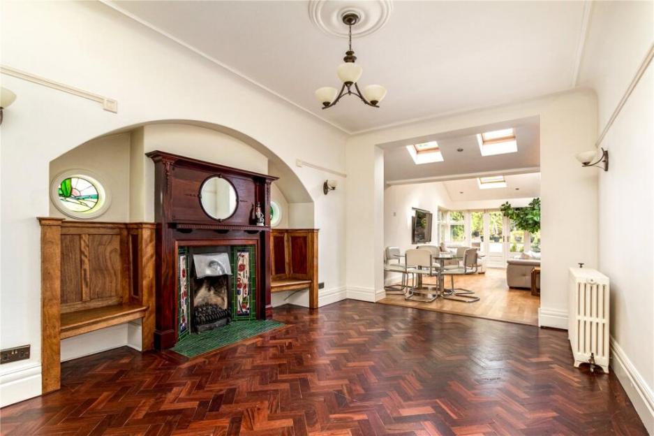 An empty living room with dark wood herringbone flooring, a large fireplace with tiled details, and an adjacent dining area leading to a sunroom.