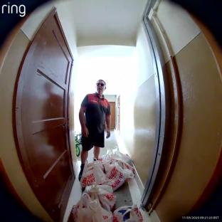 A delivery person standing in a hallway with several grocery bags at their feet.