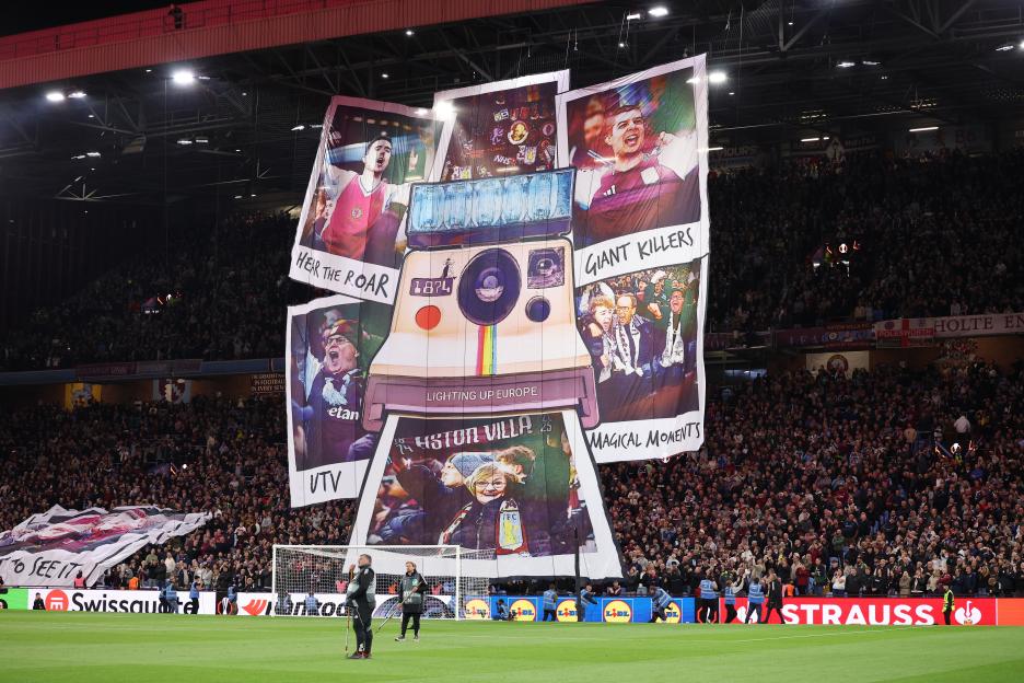 Tifo featuring a large Polaroid camera with images of fans and players, banners reading "Hear the Roar," "Giant Killers," "Lighting Up Europe," and "Magical Moments" at a football match.