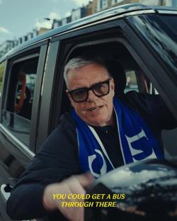 Man in a car wearing a Chelsea scarf.