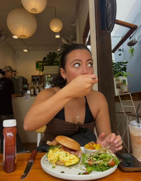 Woman eating a bagel sandwich and salad in a cafe.