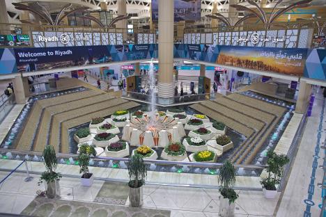 Interior view of King Khalid International Airport in Riyadh, Saudi Arabia, featuring a central fountain surrounded by plants.