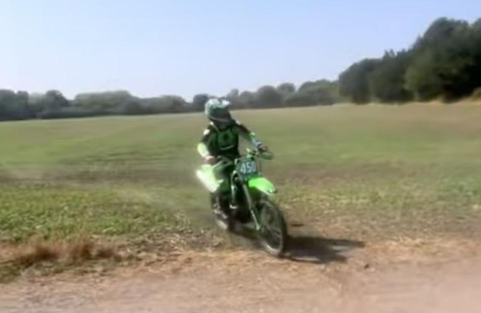 A motorcyclist on a green dirt bike rides across a field.