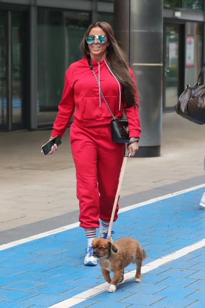 Katie Price wearing a red tracksuit and blue sunglasses, walking a small brown dog on a leash.