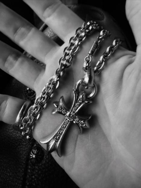 Hand holding a silver cross pendant on a chain.