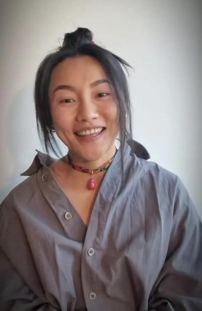 Nancy Xu smiling while wearing a gray shirt and a colorful necklace with a pink pendant.
