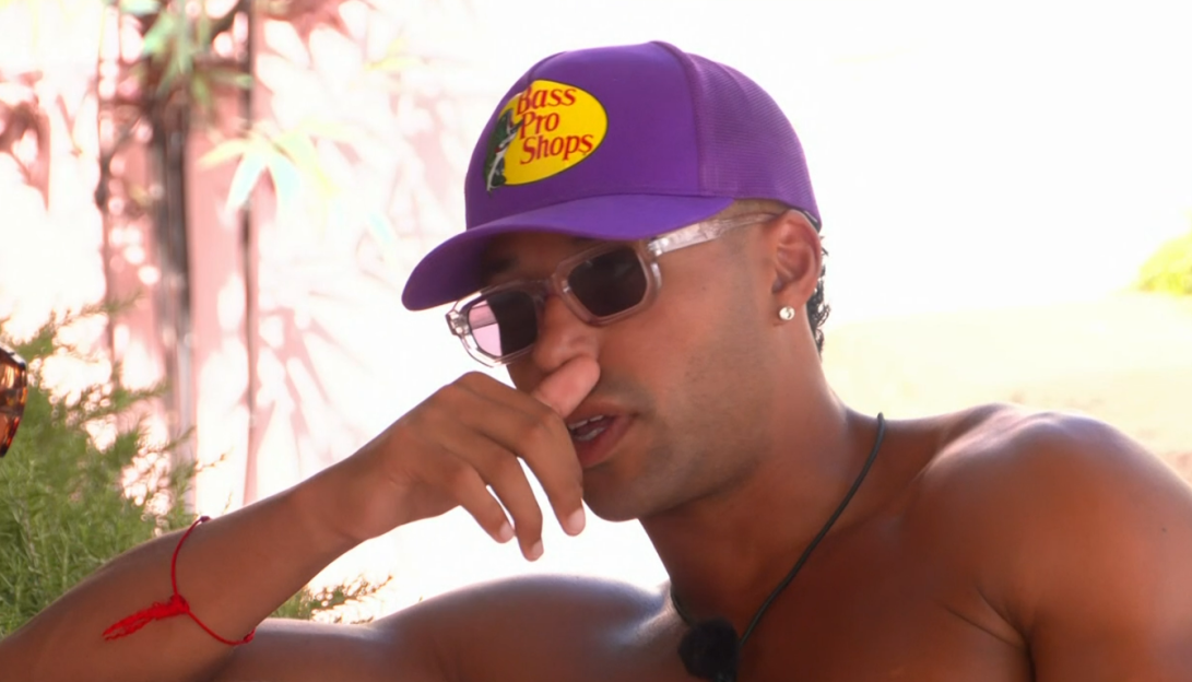 Man wearing a Bass Pro Shops hat and sunglasses, looking thoughtful.