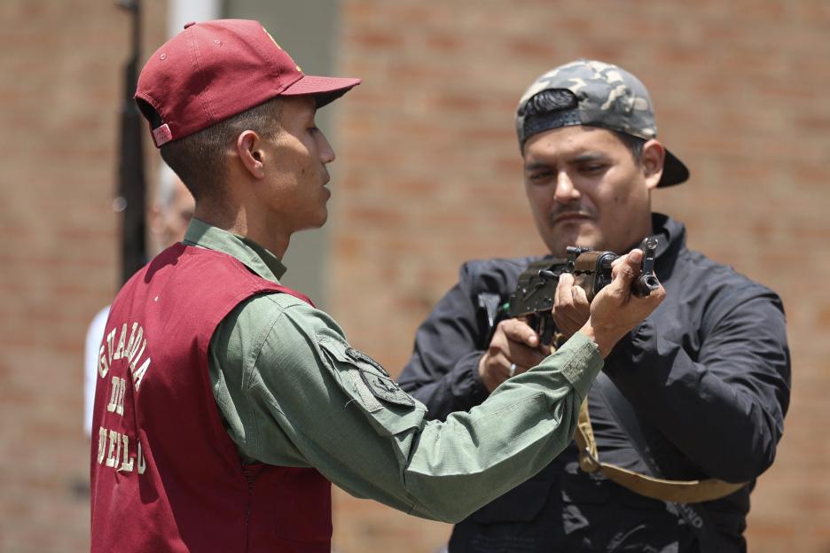 A man in a red vest and red cap giving instructions on holding a rifle to another man in a black jacket and camouflage cap.
