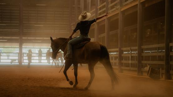 Cowgirl riding horse in arena, pointing.