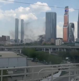 Smoke billowing from a building, people behind barriers watching.