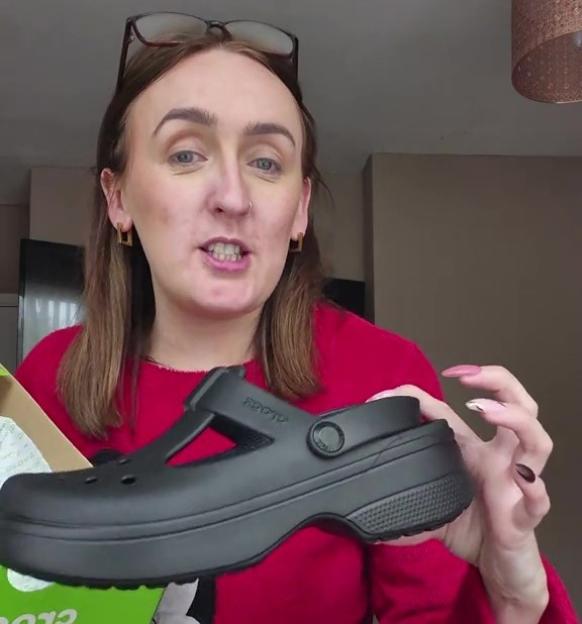 Woman holding up a black Croc shoe.
